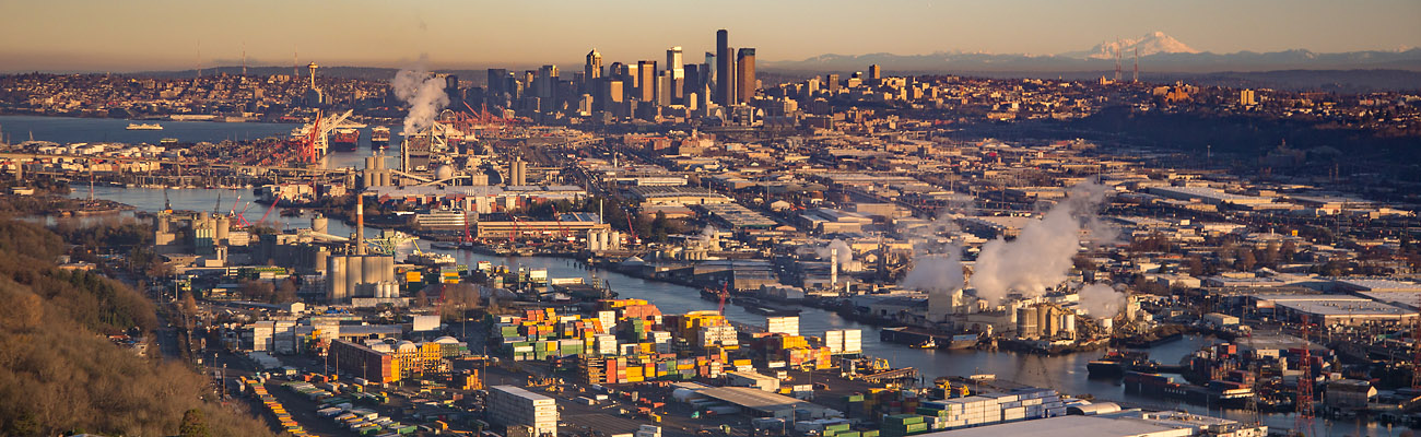 Aerial view of downtown Seattle, SODO, and the Lower Duwamish Waterway. This photo is looking North and shows Mount Baker in the background and the Space Needle. Industry and containers line the waterway.