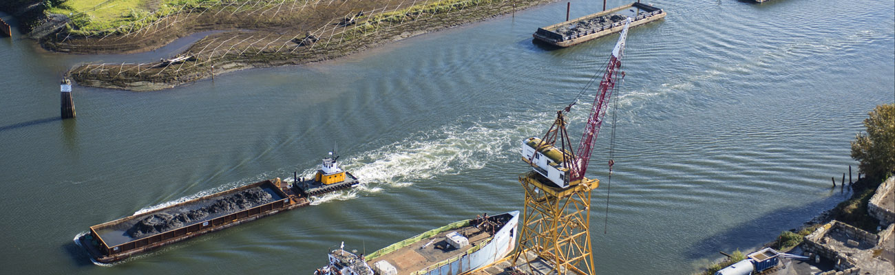 Aerial view of the Duwamish River near Boeing's Plant 2 cleanup. Photos shows two barges traveling on the river, with one being pushed by tugboat. Photo also shows a yellow crane on the banks of the waterway.