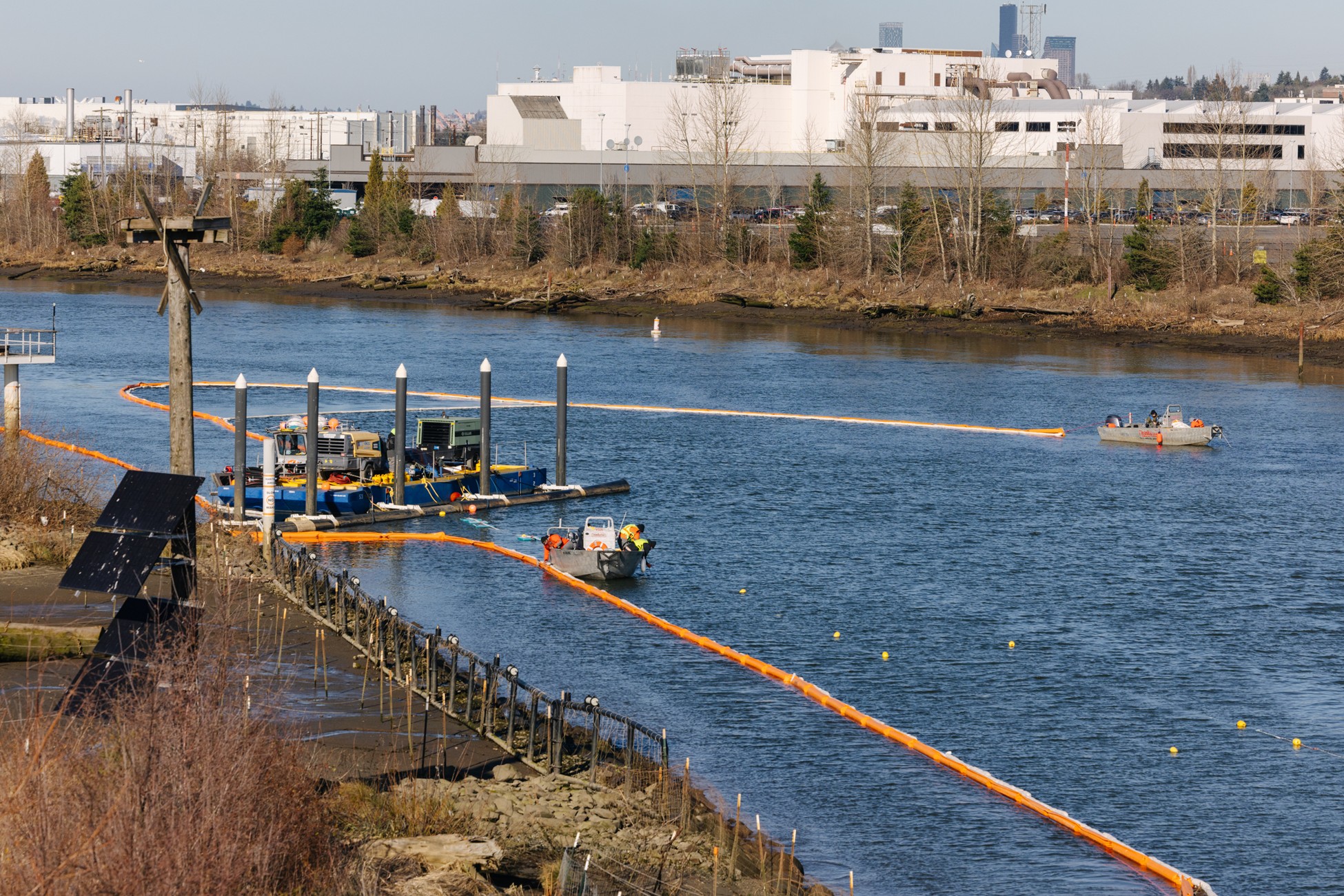 2026_0123 SMA12b Sheen capture tech (PC King County) Photo showing sheen recovery crews adjusting and maintaining oil-containment booms and bubble curtain used to capture and manage sheens observed as a result of dredging SMA 12B. Image shows three vessels, a boom on the water, and building in background. Looking north.